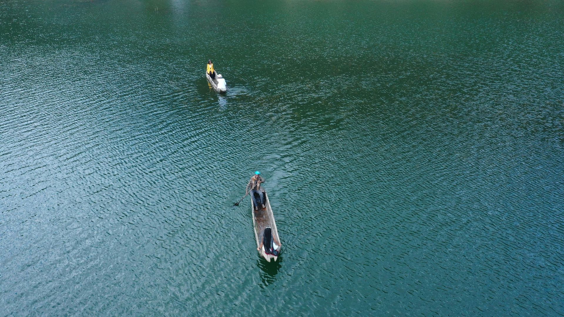 Two boats on a blue-green lake. One is a kayak, and the other is a long boat.