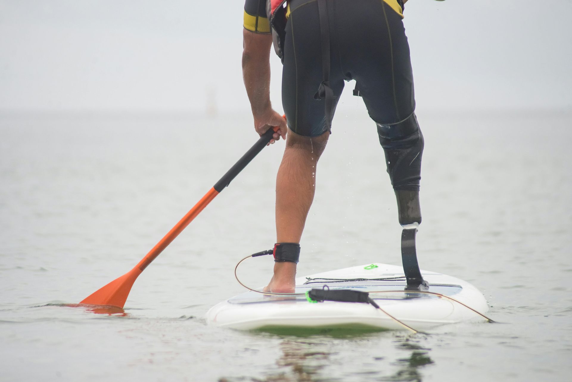 Person with prosthetic leg paddleboarding in water.