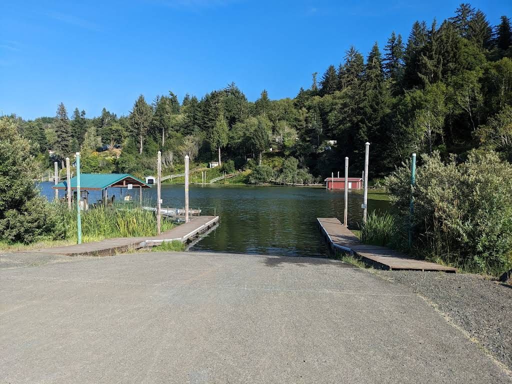 Boat ramp leading to a lake, docks on either side, trees and foliage in the background under a blue sky.