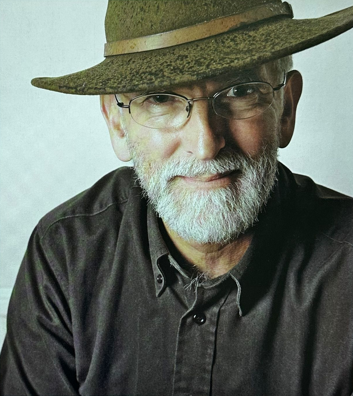 Portrait of a bearded man in glasses and a brown hat, wearing a dark shirt, against a plain background