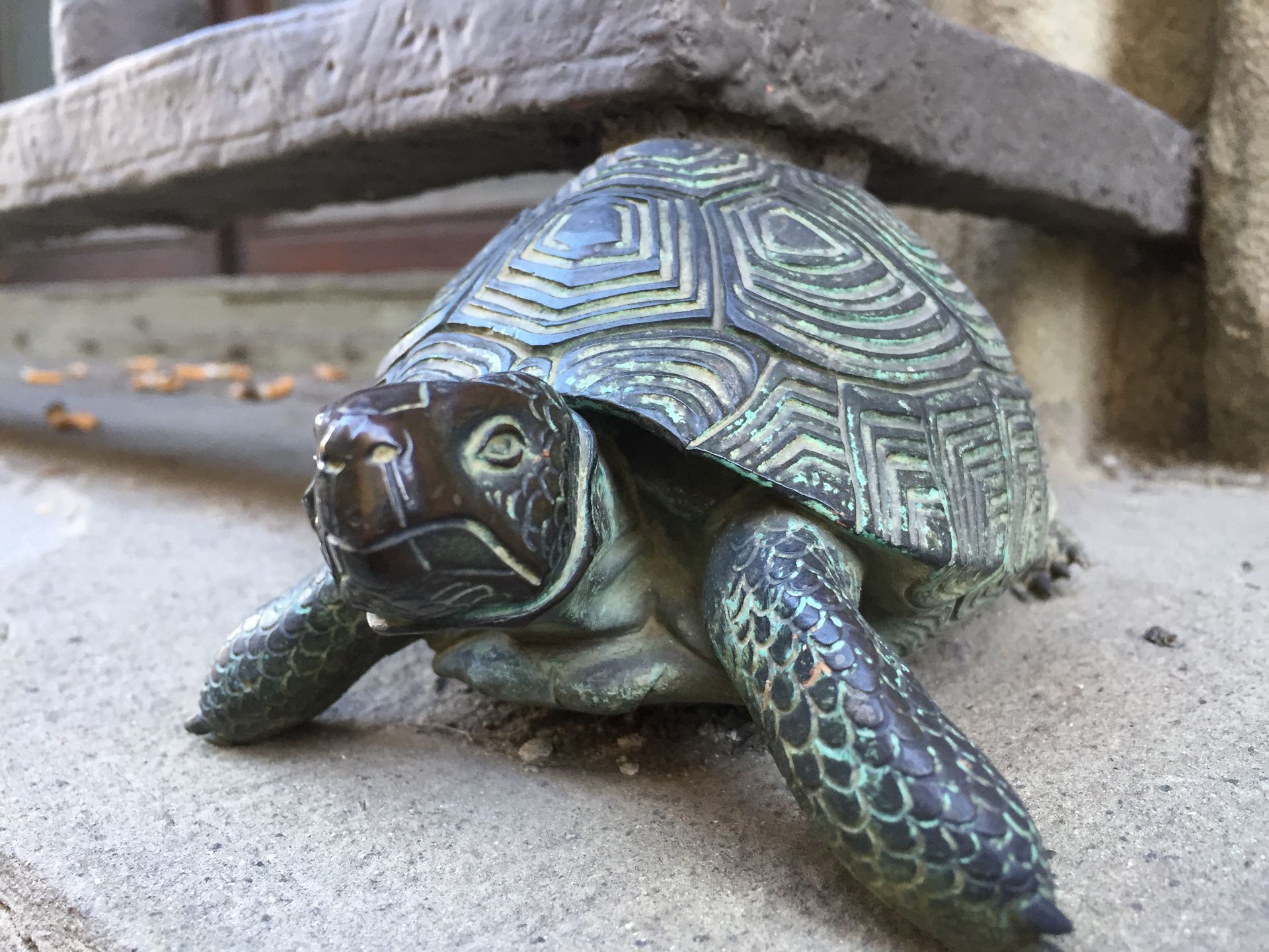 Turtle sculpture on a concrete ledge, with patterned shell and greenish legs