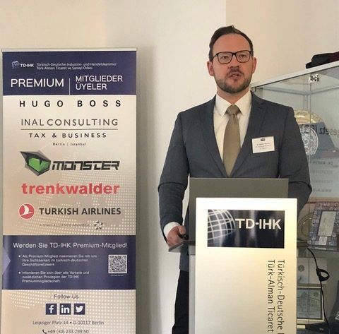 Ein Mann am Podium mit dem Logo „TD-IHK“ neben einem Banner mit Sponsoren und Logos.