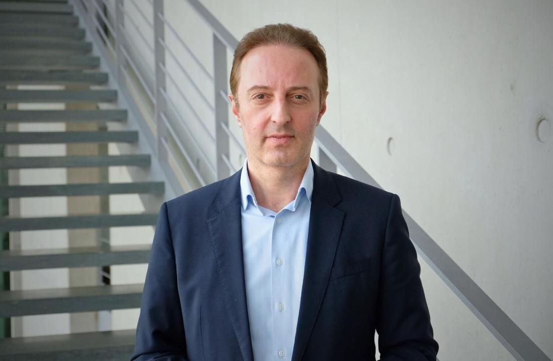 Ein Mann in blauem Hemd und Blazer steht in der Nähe einer Treppe.