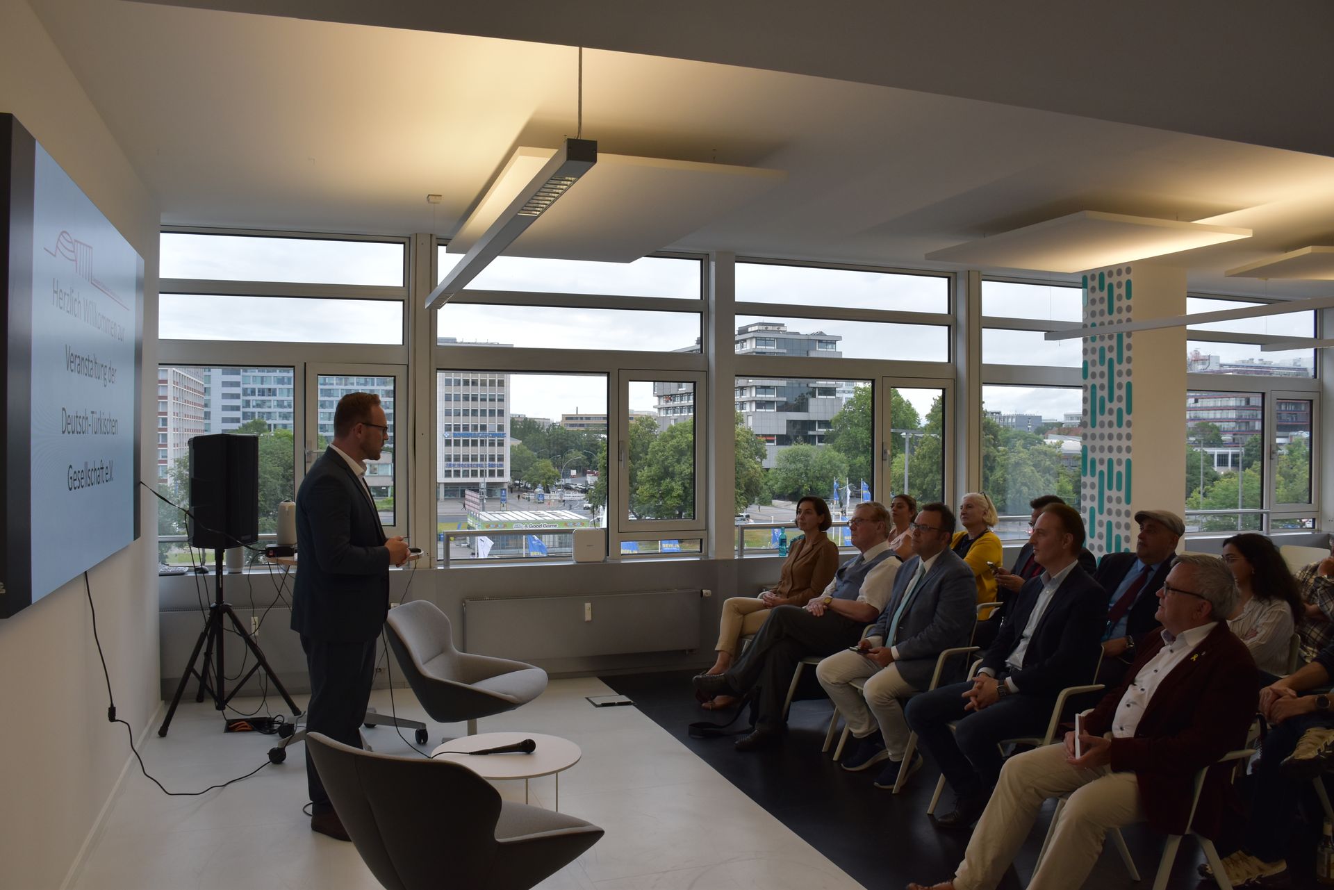 Ein Mann präsentiert vor Publikum, im Hintergrund ein großes Fenster.