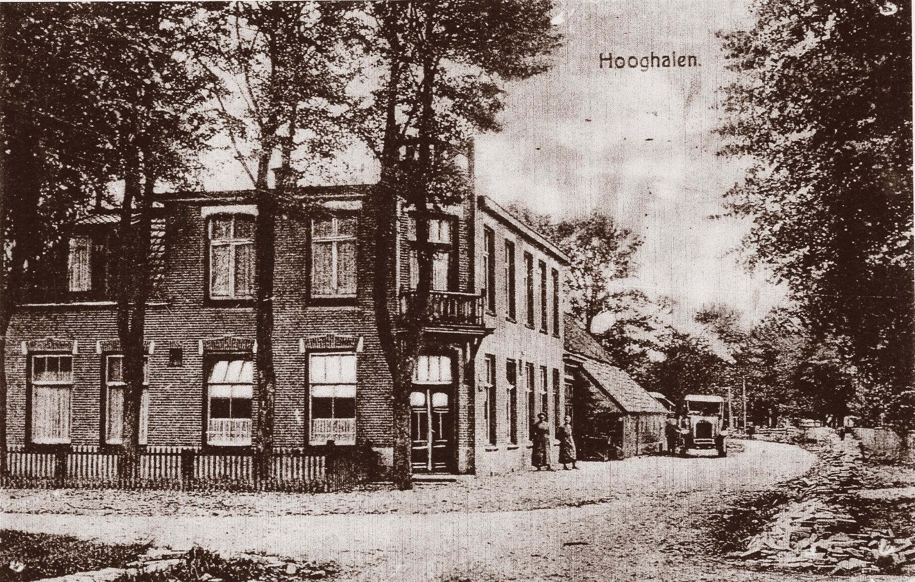 Oud, sepiakleurig gebouw met een balkon en hoge bomen langs een weg; mogelijk een hotel.