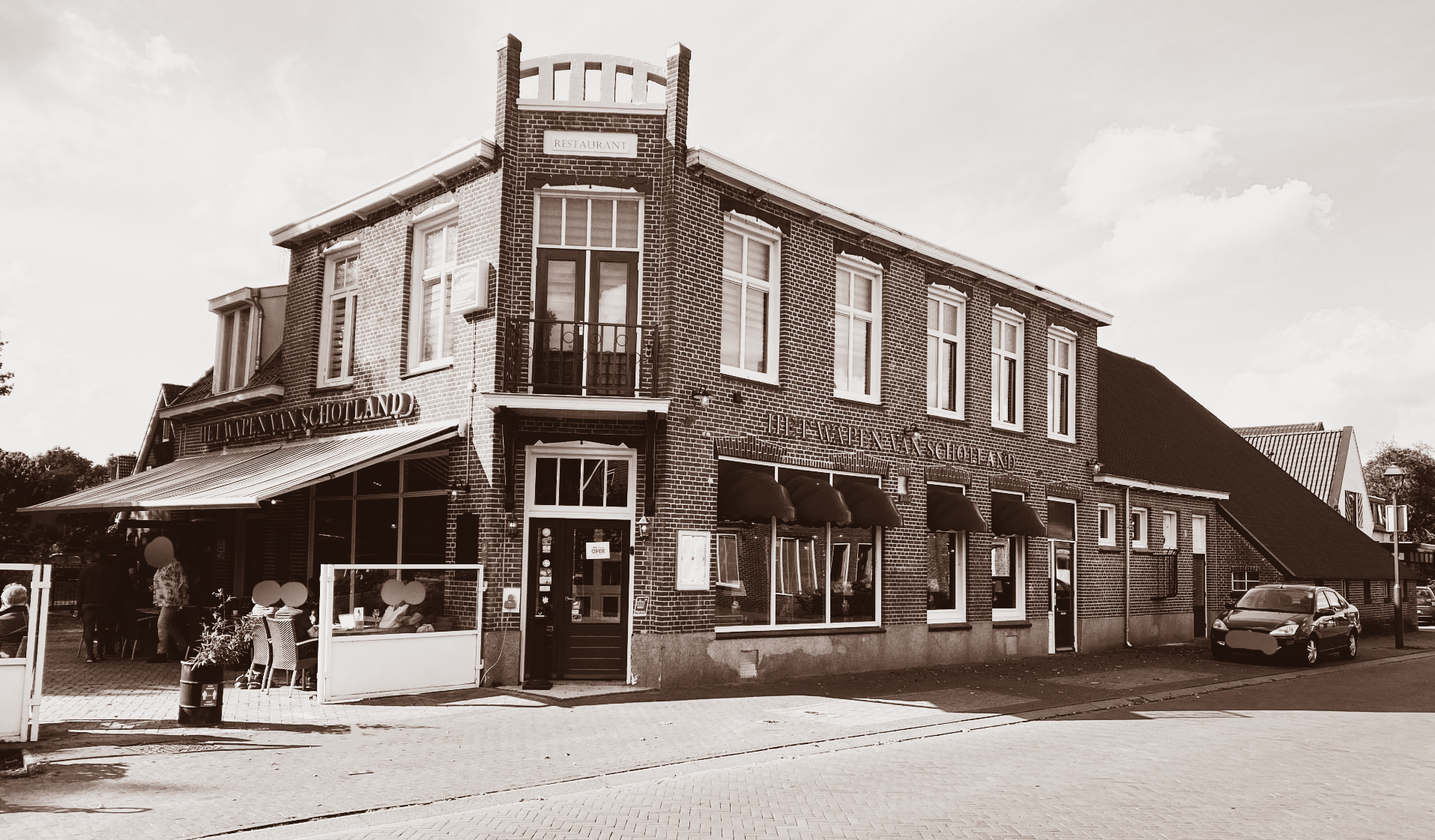 Bakstenen gebouw met luifel boven de winkelpui. Auto geparkeerd in de buurt.