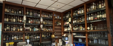 Schappen vol flessen in een bar. Bruine houten planken, een bar en glazen zijn zichtbaar.