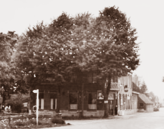 Een hoekpand in sepiatinten, deels aan het zicht onttrokken door bomen, mogelijk een pub met uithangborden en een terras.