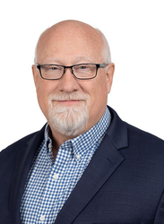 Headshot of a bald man with glasses, white goatee, and navy blazer over a blue checkered shirt.