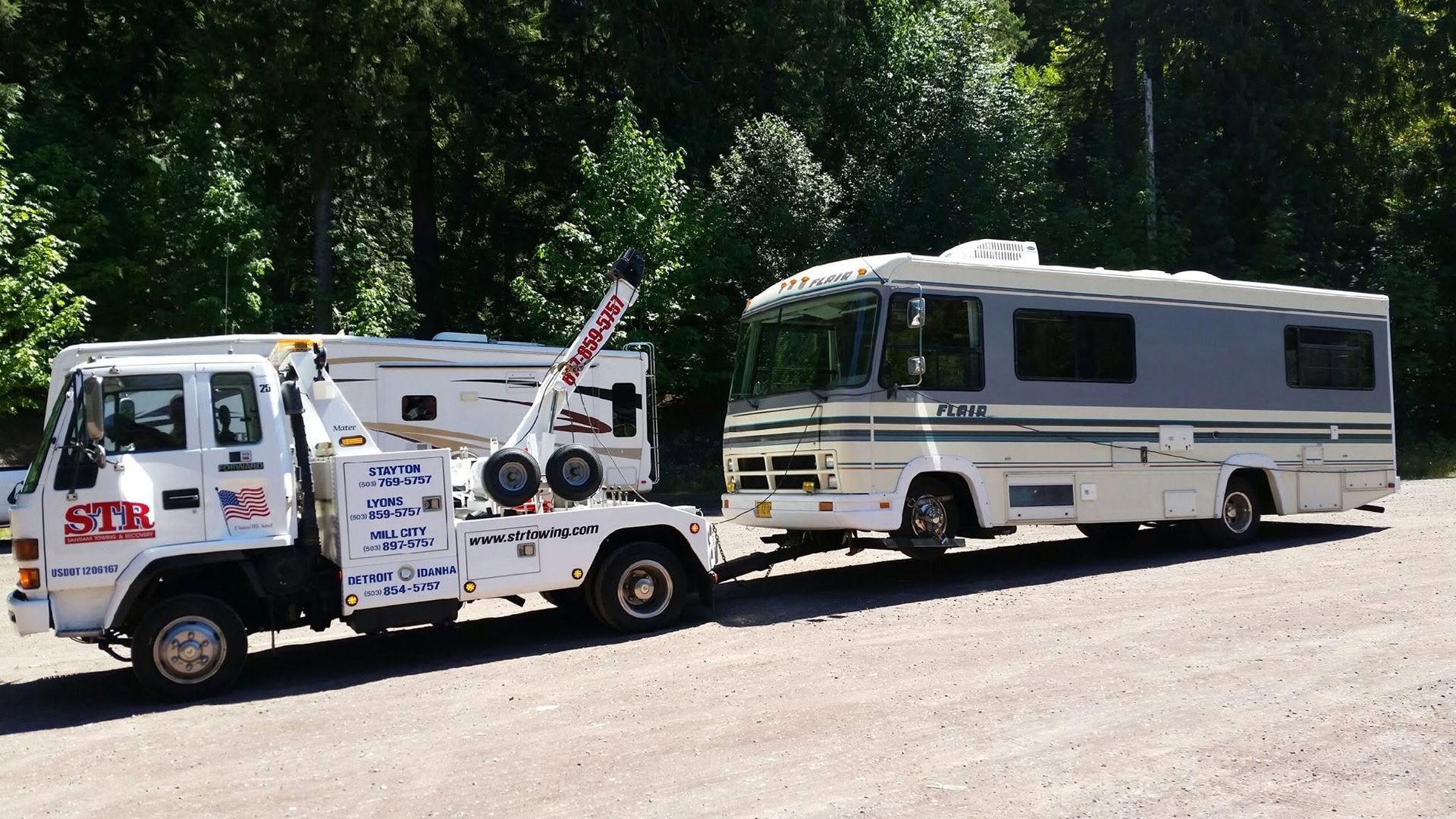 Tow truck hauling a white RV on a tree-lined road