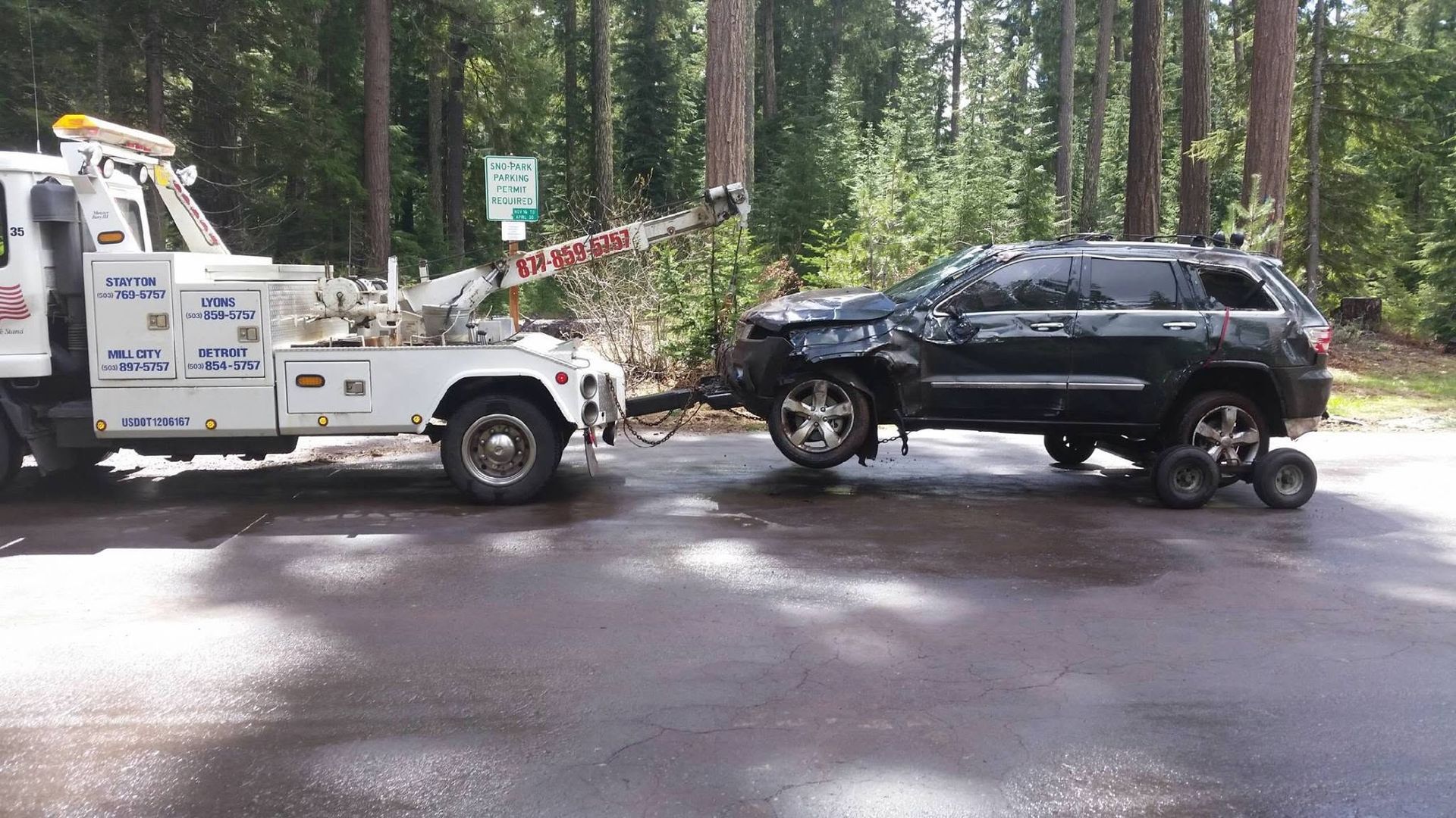 Tow truck towing a black SUV on a wet road in a wooded area