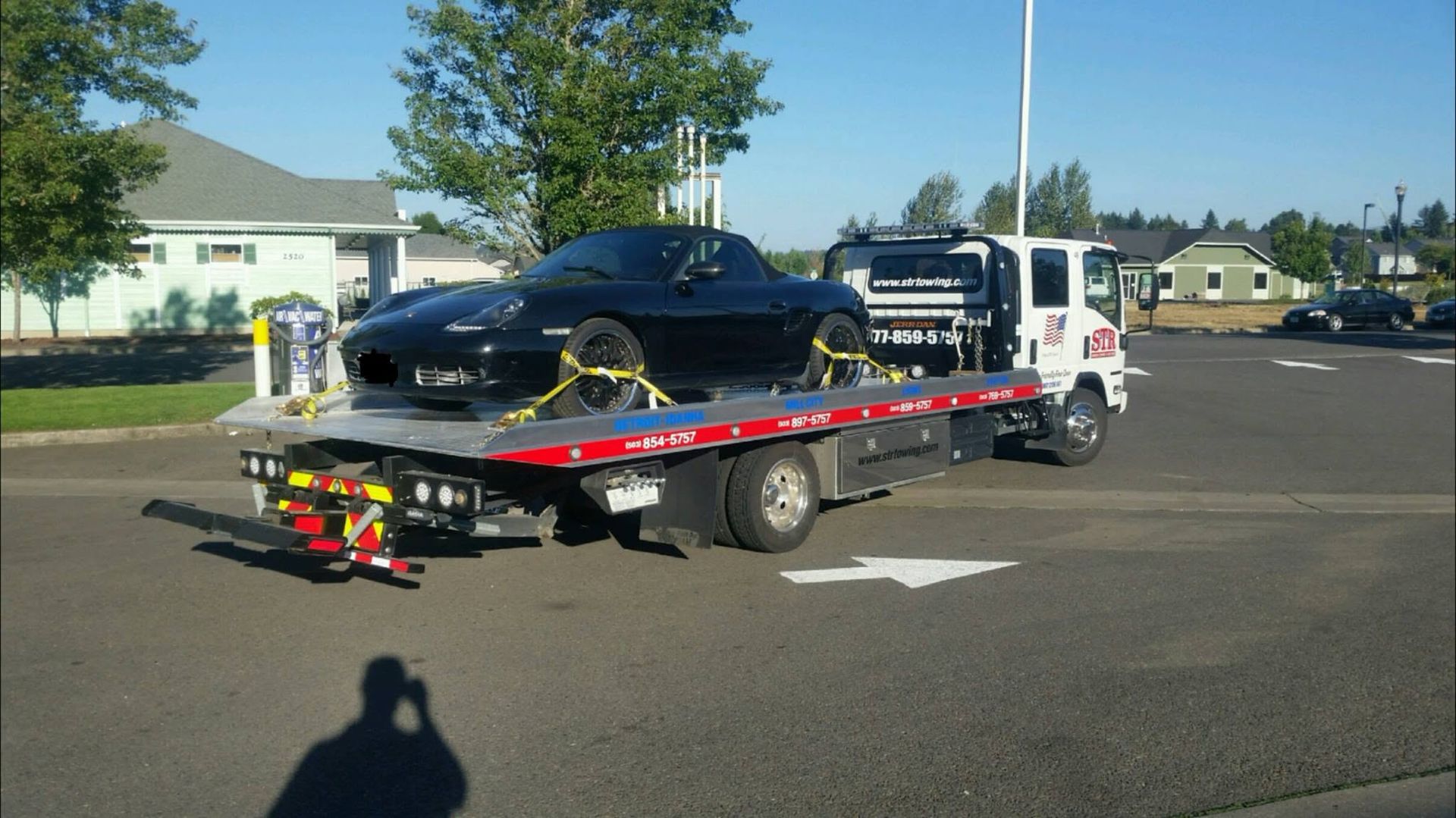 Tow truck carrying a black sports car on a flatbed in a residential street