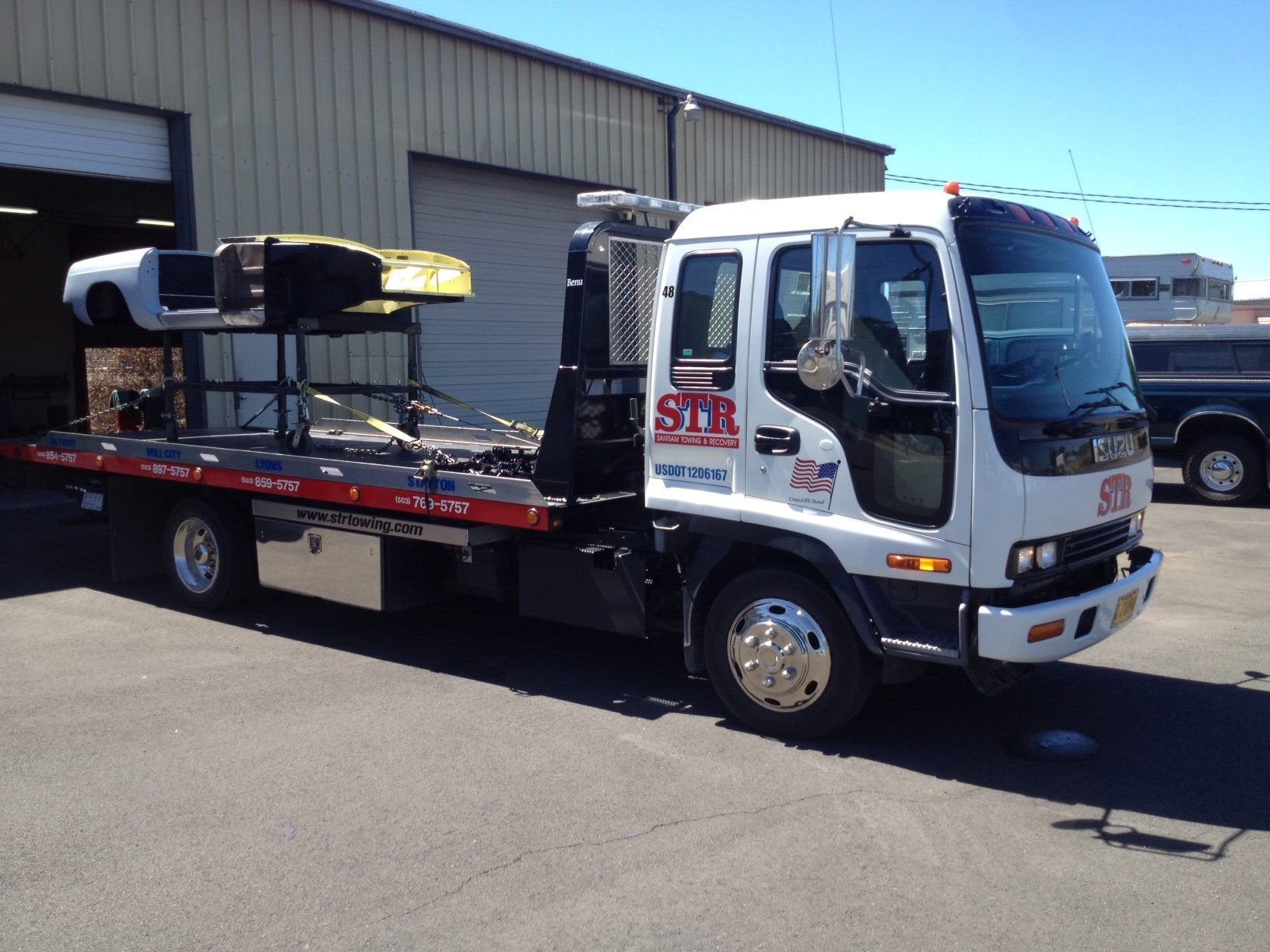 White flatbed tow truck parked outside a warehouse on a sunny day