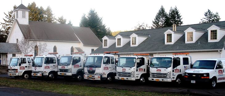 Line of white utility vans parked in front of a white church and trees