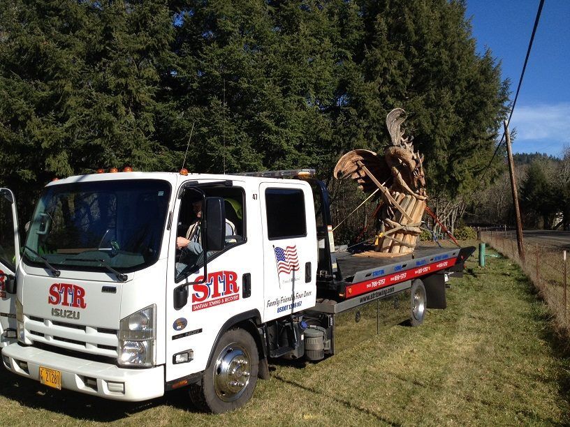 White flatbed truck hauling a large tree root ball along a rural roadside with trees and power lines