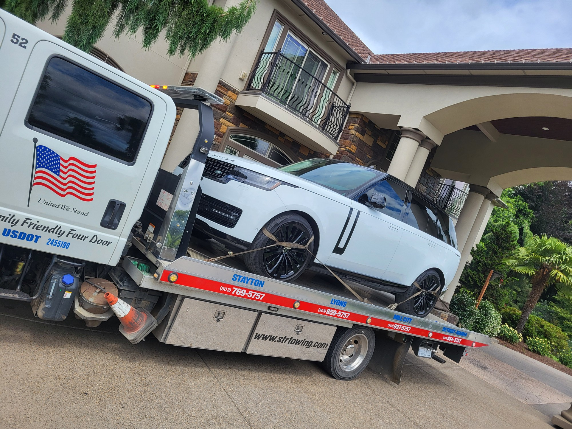 Tow truck hauling a white sports car on a flatbed in front of a building entrance