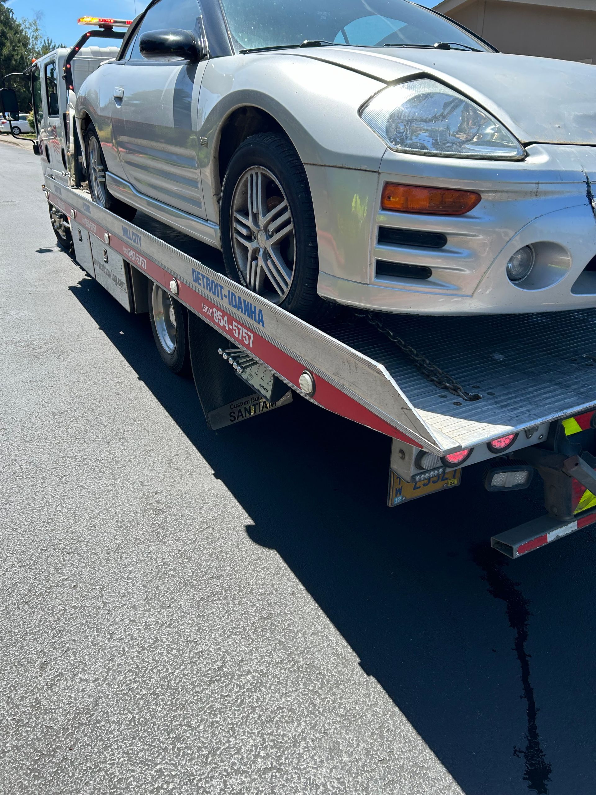 Silver sports car on a flatbed tow truck on a sunny road