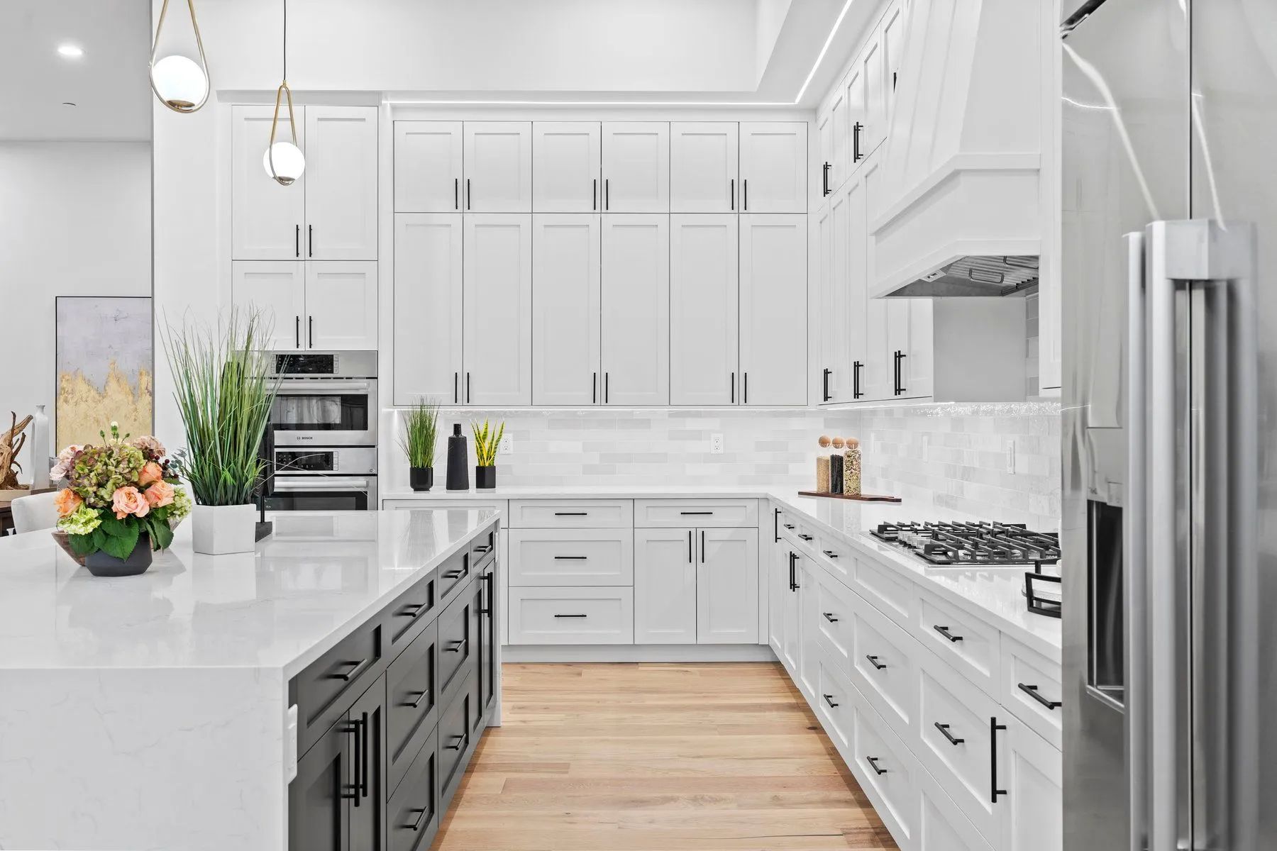 Bright white modern kitchen with island, black stools, stainless fridge, and wood floor.