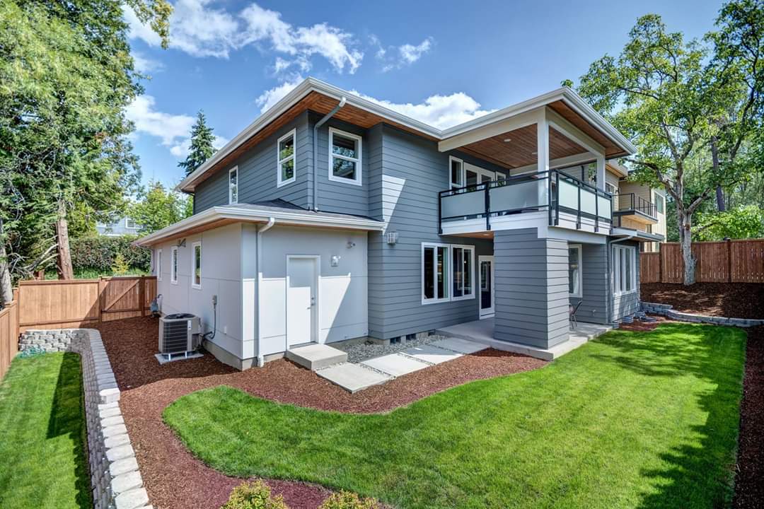 A large gray house with a large lawn in front of it.