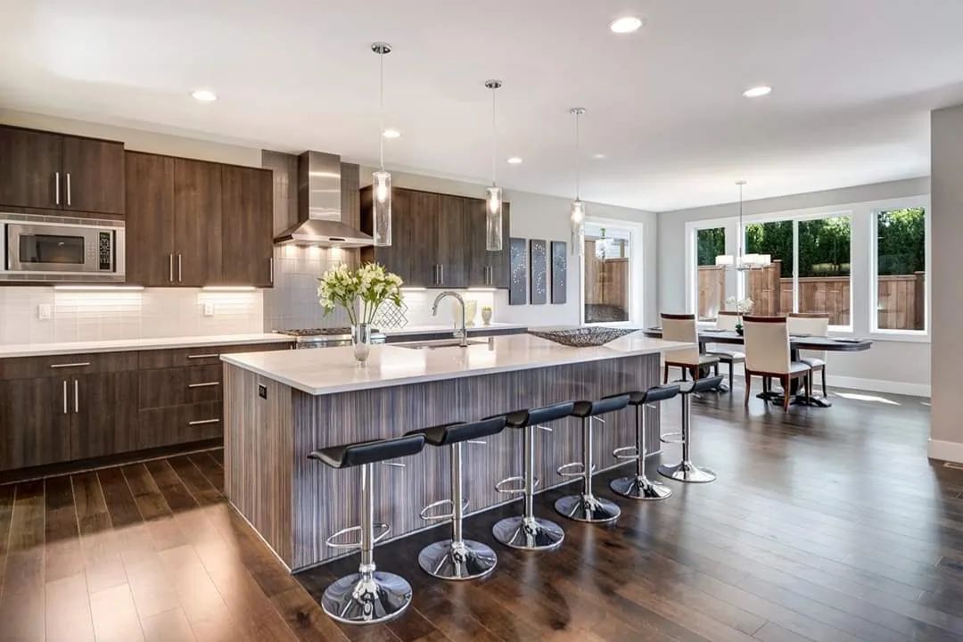 Modern kitchen with wood cabinets, large island, bar stools, and bright dining area by windows