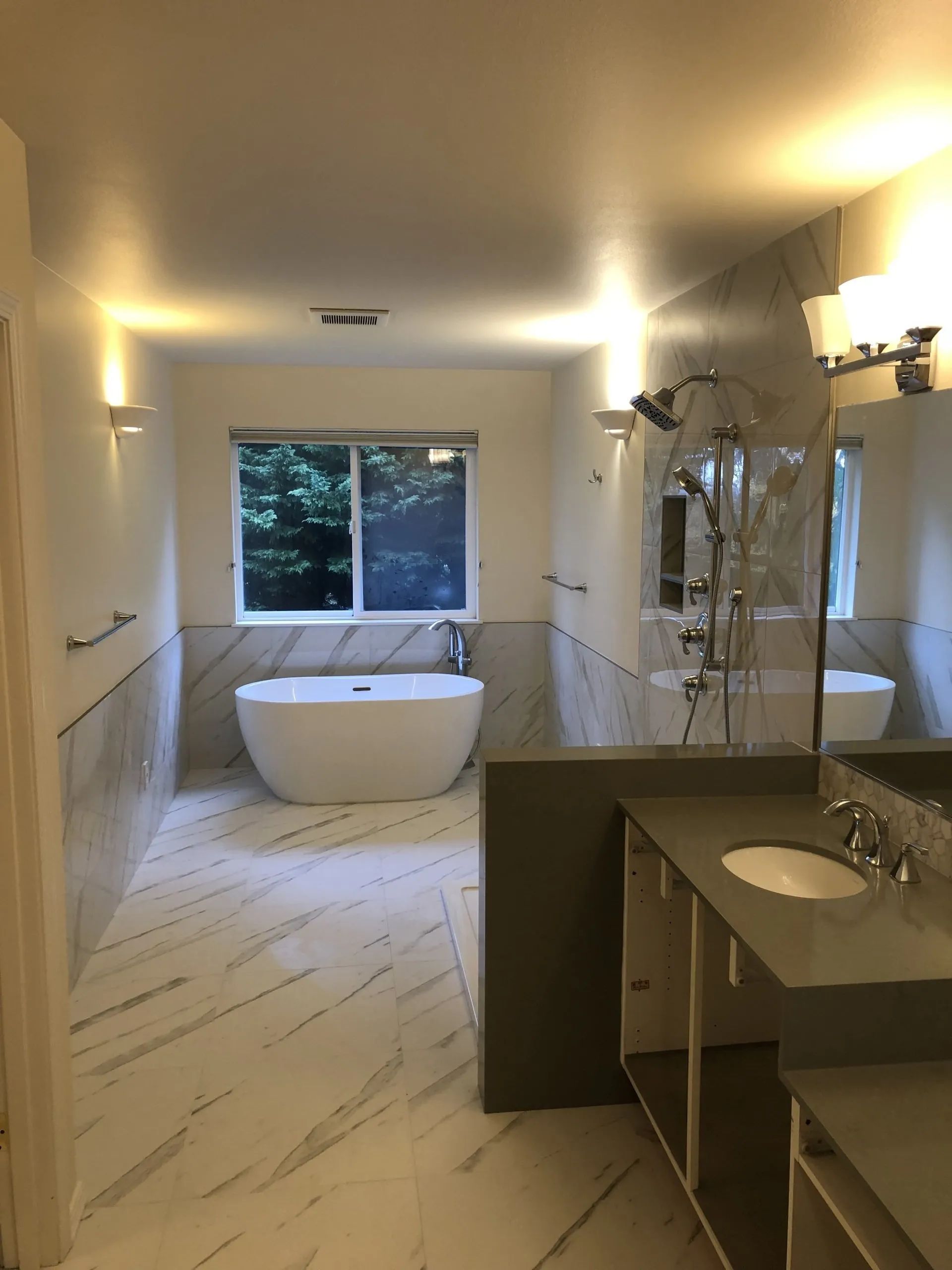 Modern bathroom with a freestanding tub, large window, glass shower, and double vanity under warm lights