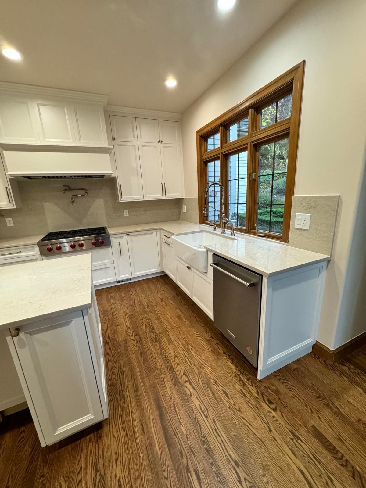 A kitchen with white cabinets , hardwood floors , a sink , and a stove.