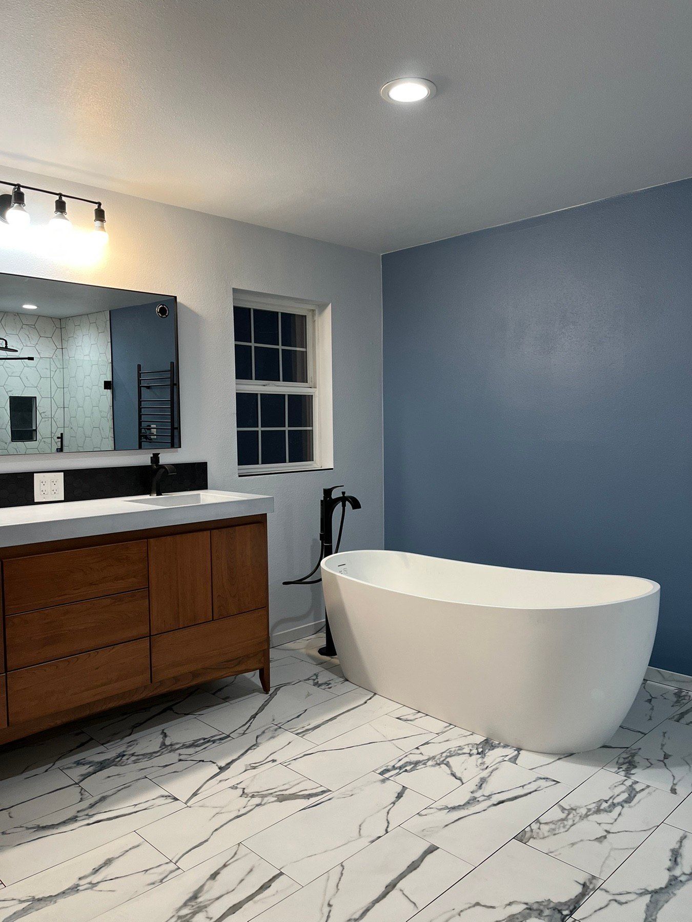 A bathroom with a bathtub , sink , mirror and marble floor.