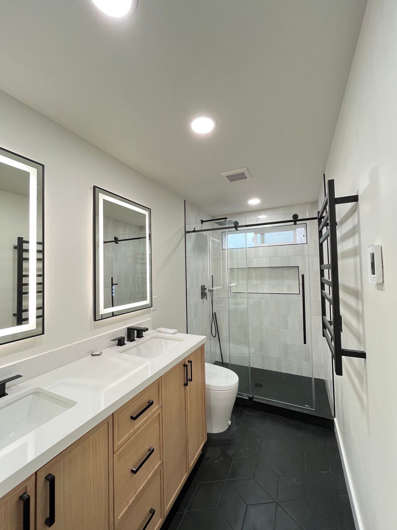 Modern bathroom with double vanity, walk-in shower, and black tile floor.