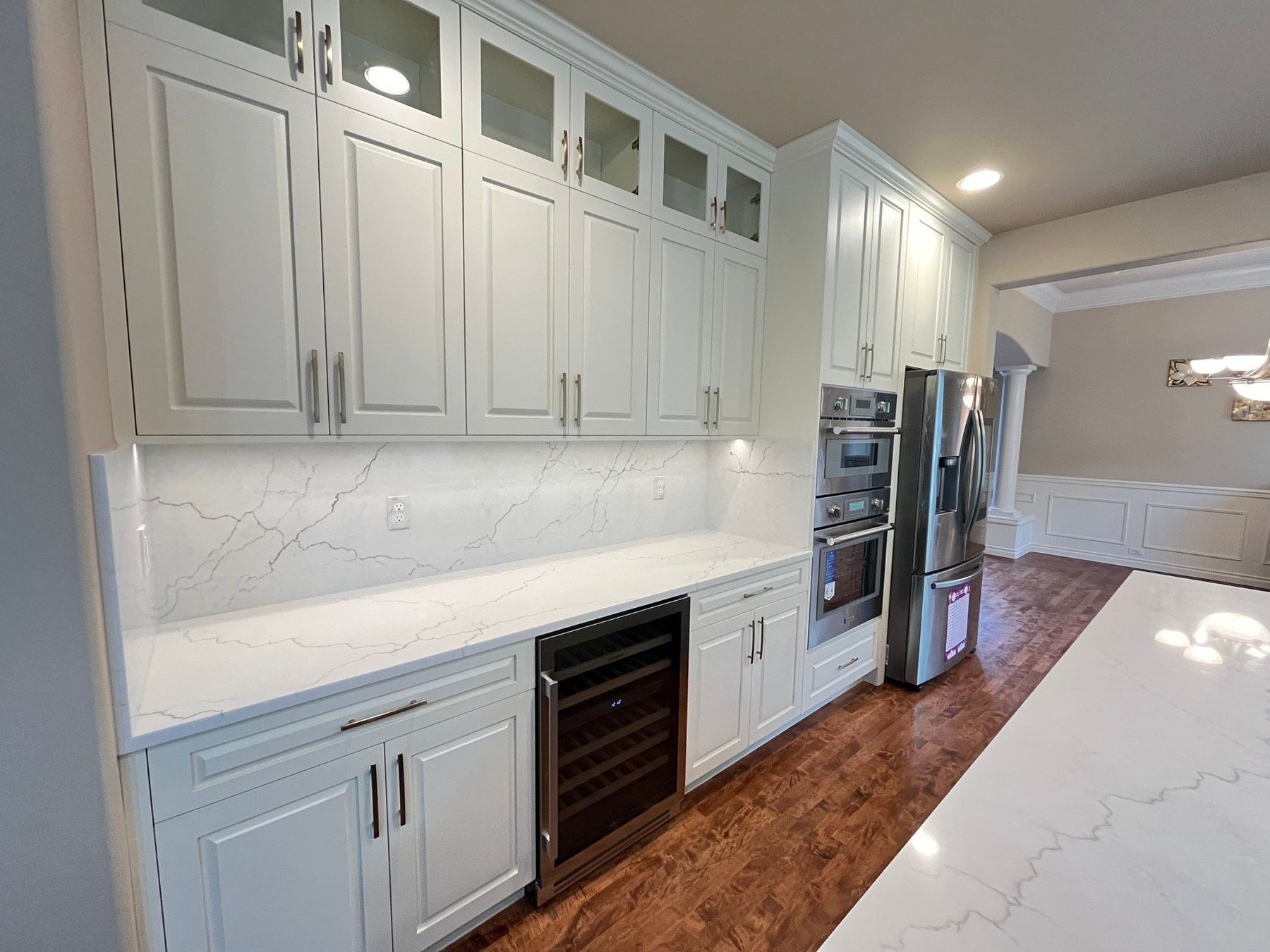 White kitchen cabinets with countertop and wine cooler. Stainless steel appliances and wood floor.