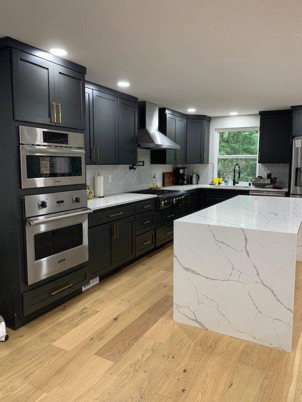 A kitchen with black cabinets , stainless steel appliances , and a large island.