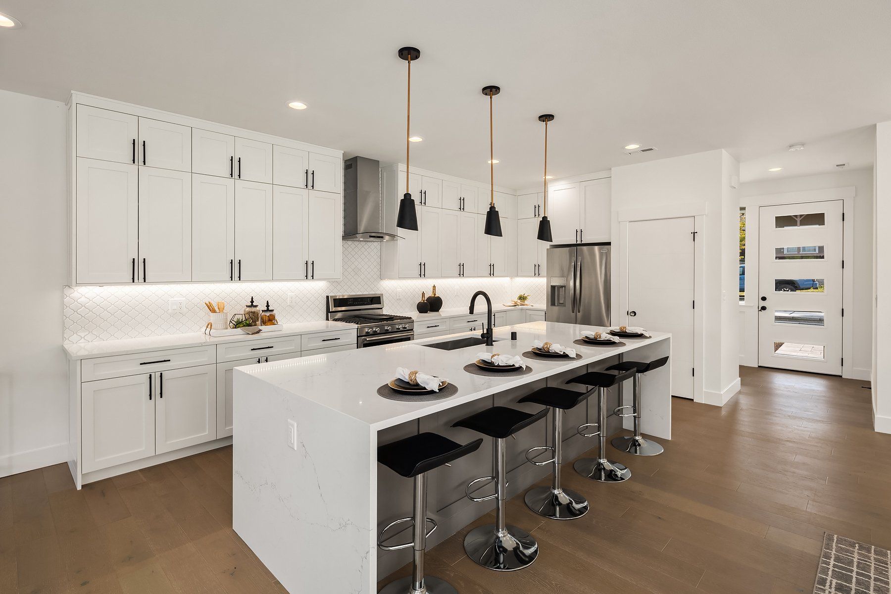 A kitchen with white cabinets , a large island , stools and a refrigerator.