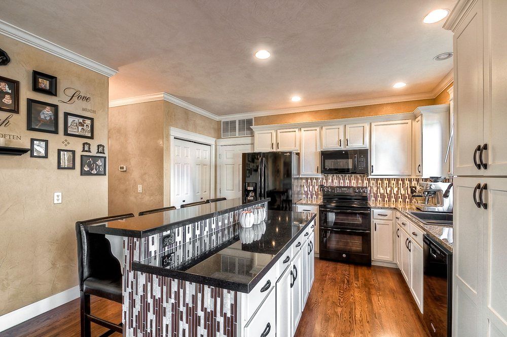 A kitchen with white cabinets , black appliances and a large island.