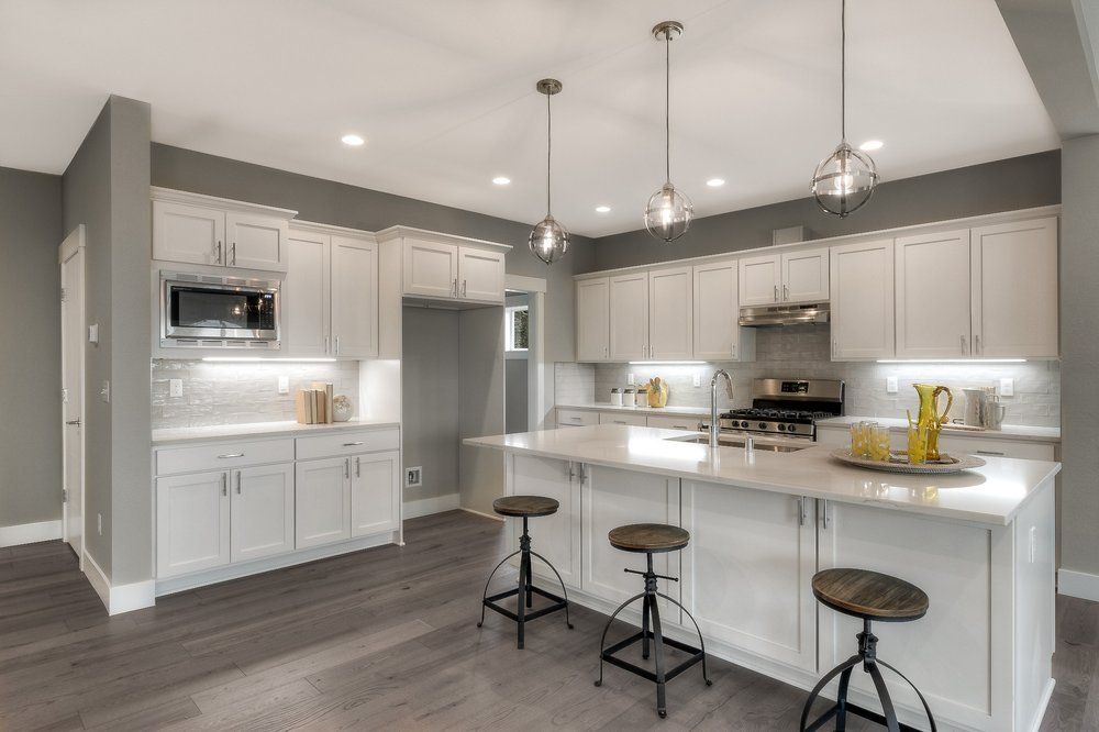A kitchen with white cabinets and stools and a large island.