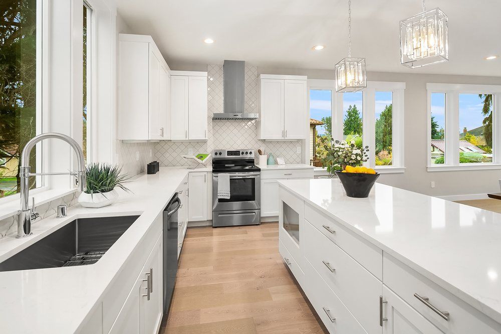 A kitchen with white cabinets , stainless steel appliances , a sink , and a large island.