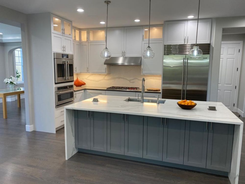 A kitchen with gray cabinets , white counter tops , stainless steel appliances and a large island.