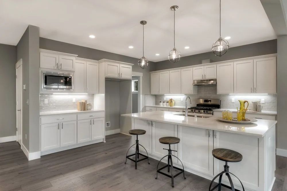 Modern white kitchen with island, barstools, stainless appliances, and pendant lighting