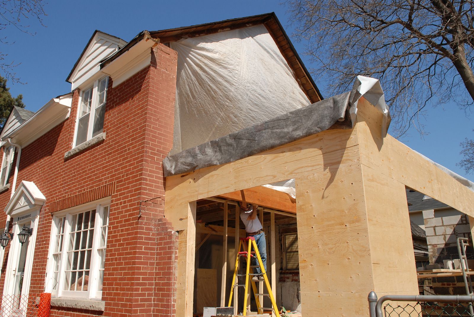 A man is standing on a ladder in front of a house under construction