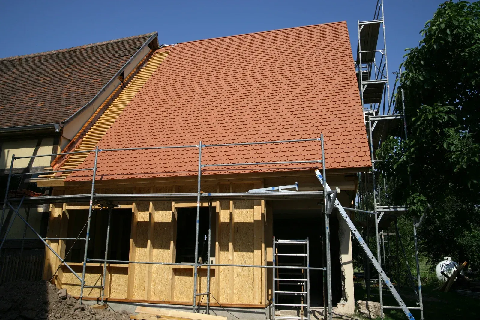 Construction of a new roof addition with orange tile, scaffolding, and wooden framing.