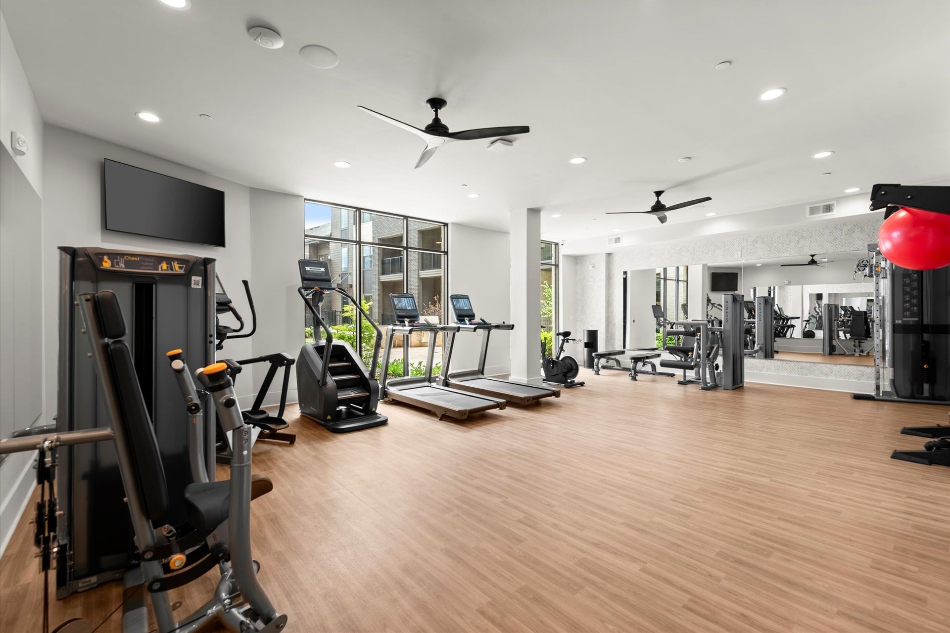 Gym with various exercise machines, wooden floor, large windows, mirrors, ceiling fans at EVOQ East Cobb Marietta, GA.