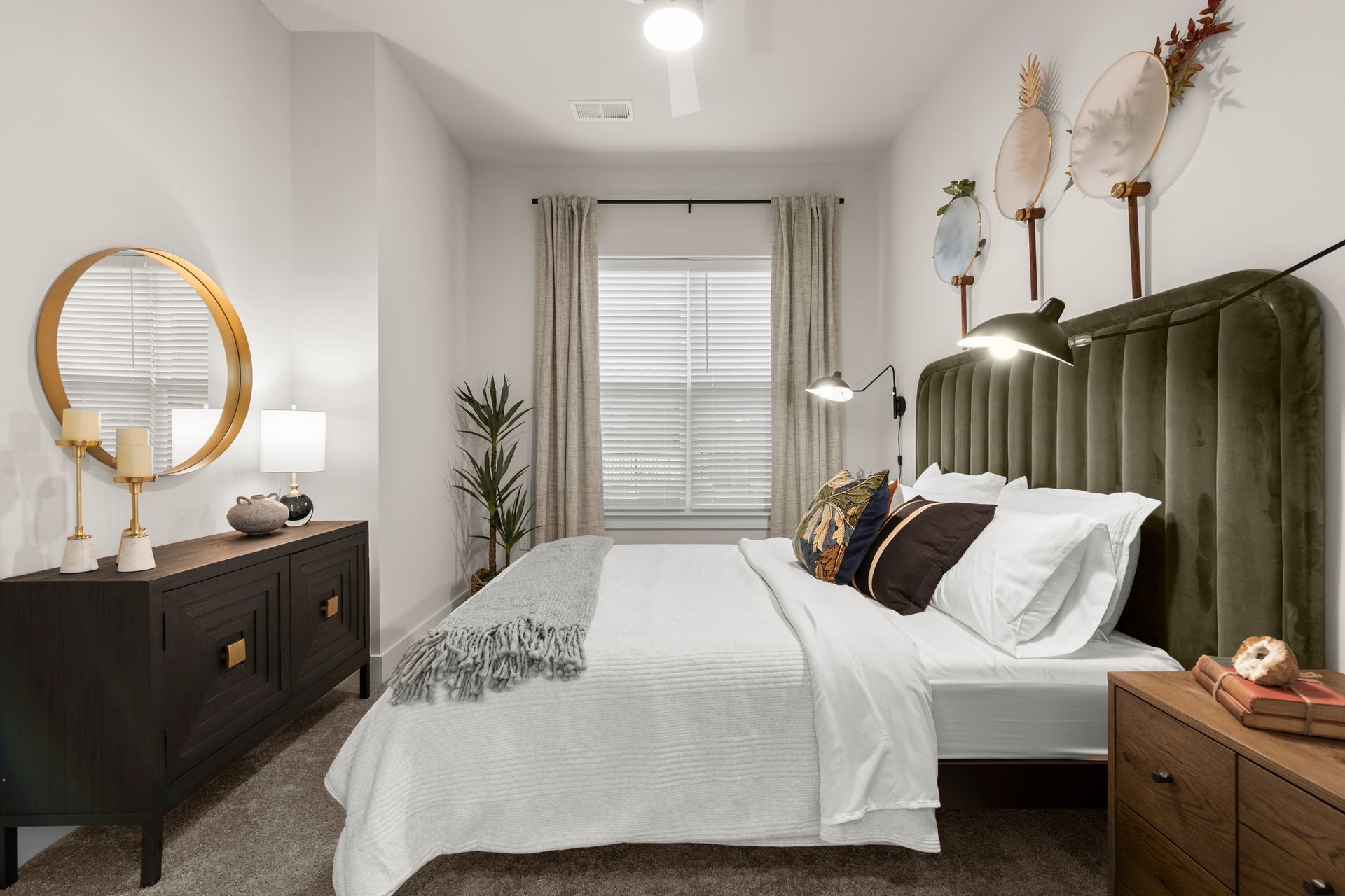 Bedroom with a green velvet headboard, a round gold mirror, and a window with blinds at EVOQ East Cobb Marietta, GA.