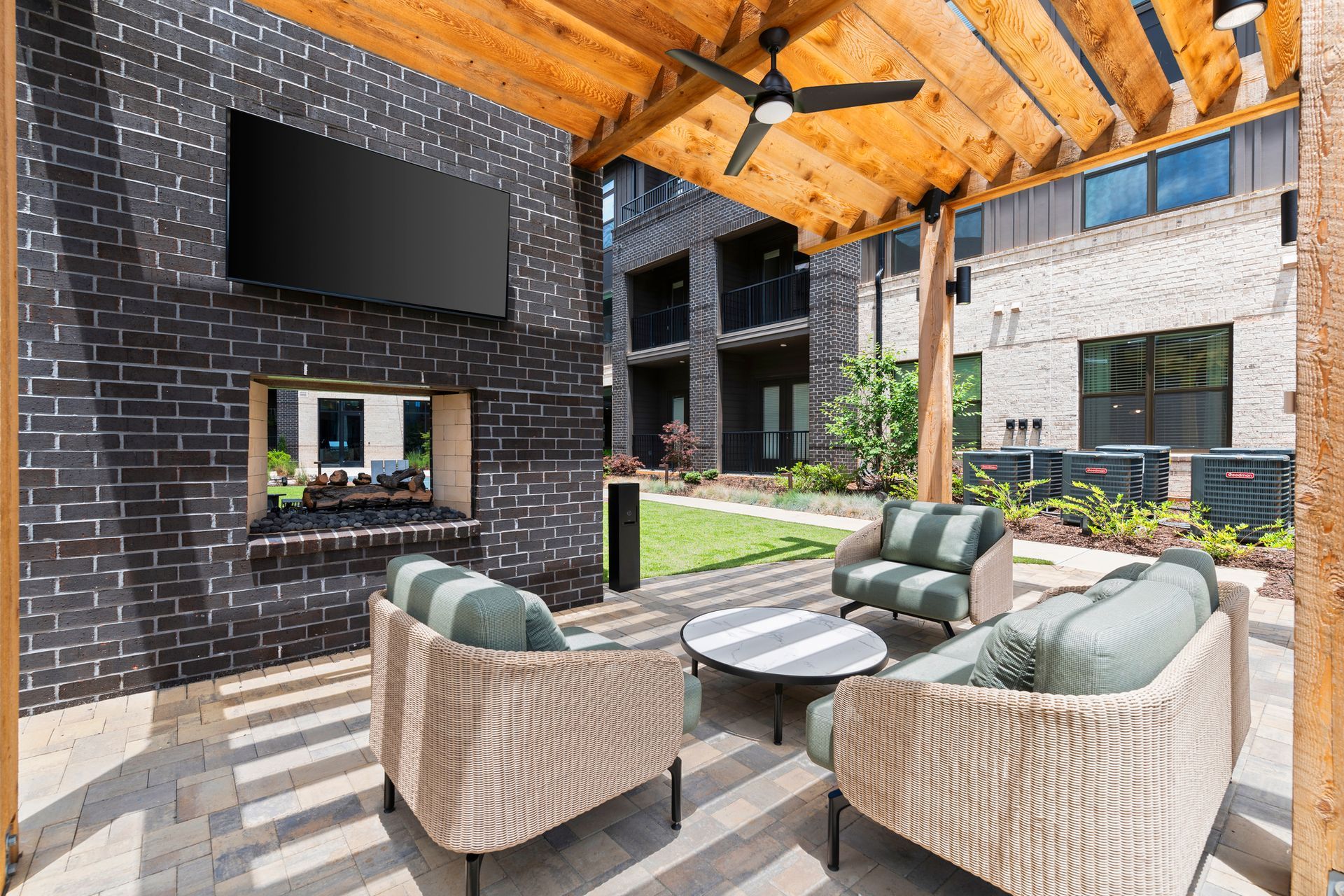Covered outdoor patio with wicker seating, striped cushions, and a large wall-mounted TV on a brick wall at EVOQ Marietta