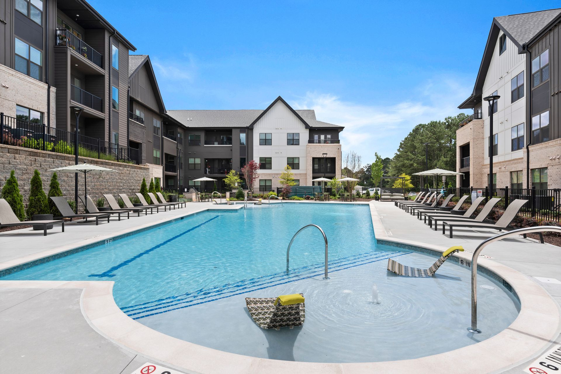 Pool and lounge chairs at apartment complex with modern architecture under a blue sky at EVOQ East Cobb Marietta, GA.