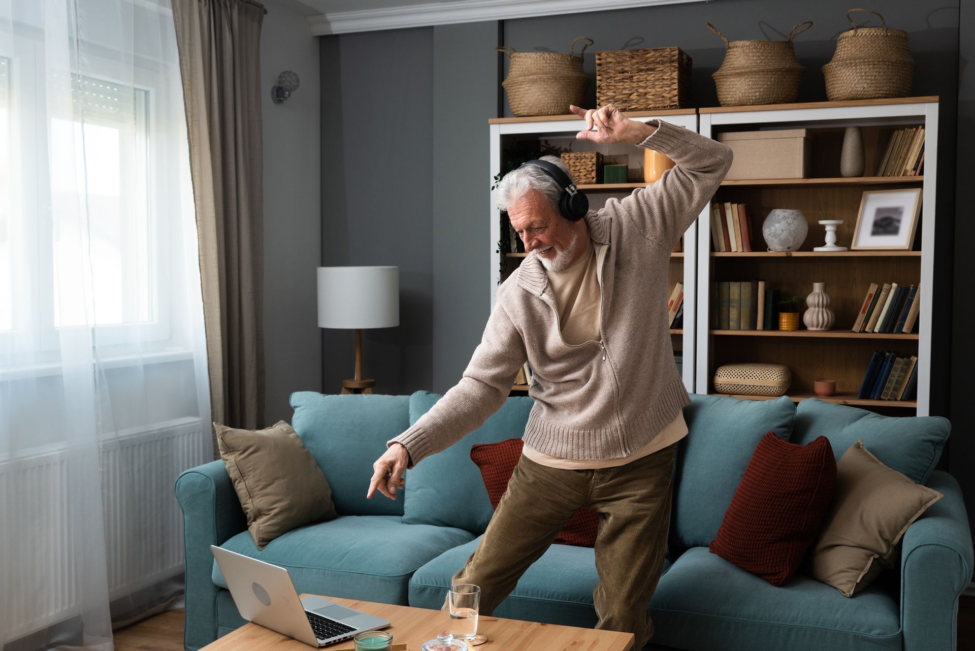 Man dancing in a cozy living room beside a blue sofa and laptop on a coffee table