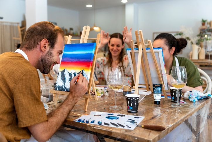 People painting at a table in an art studio, with colorful canvases and brushes at EVOQ East Cobb Marietta, GA.