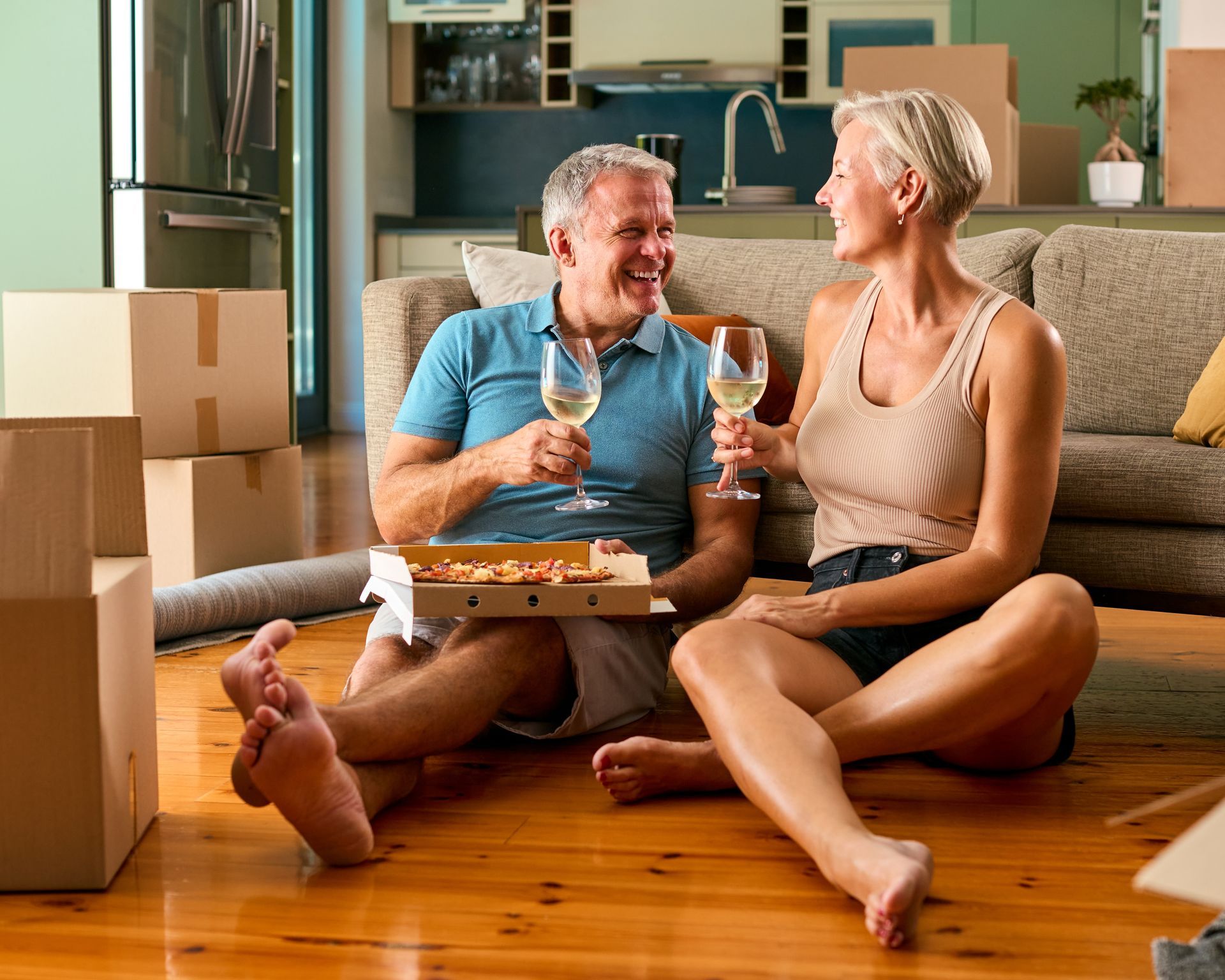 Two people sit on a wooden floor, smiling with wine glasses amid moving boxes in a living room at EVOQ East Cobb