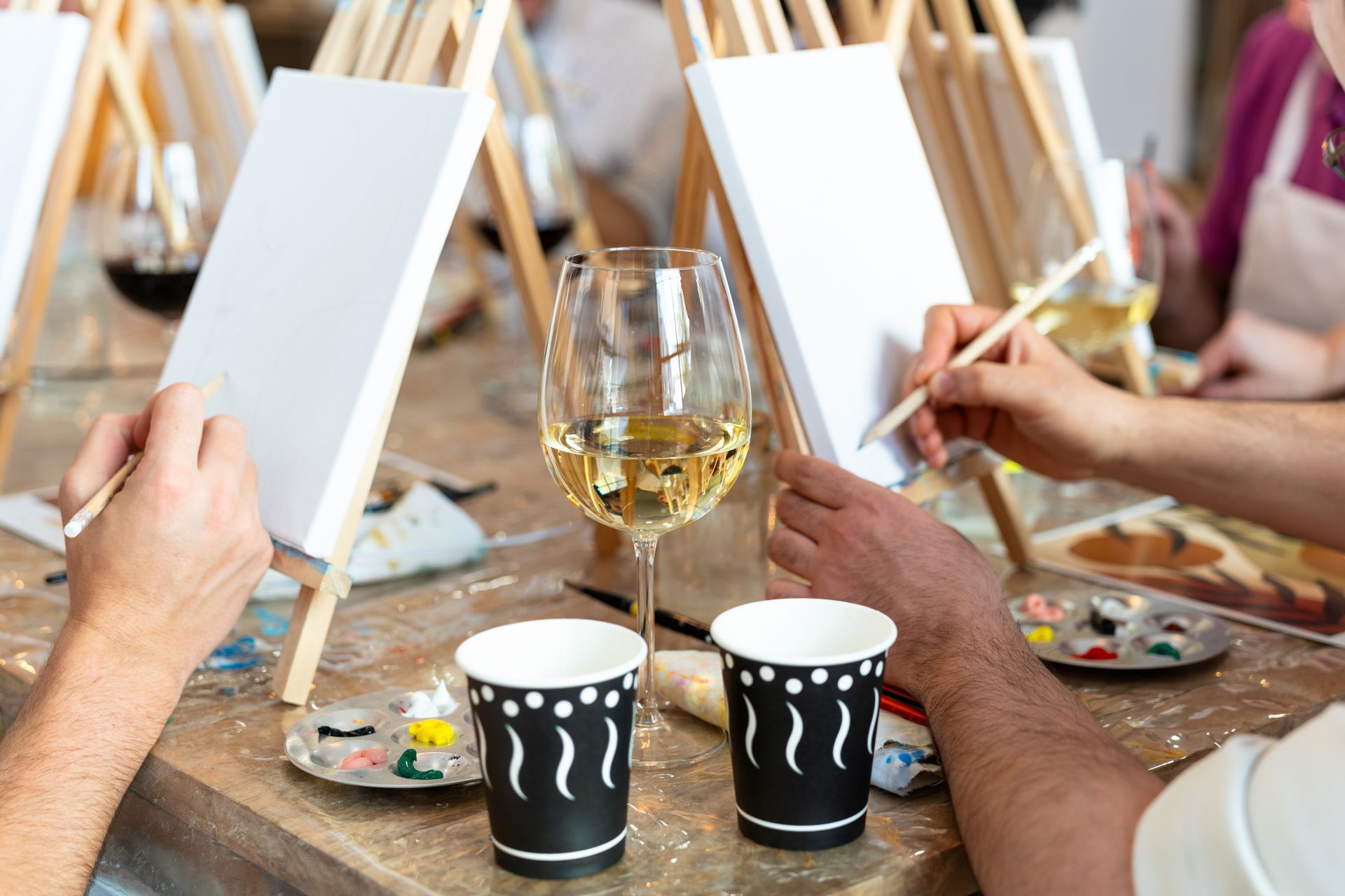 People painting on easels at a paint and sip event. Wine glass and cups on the table at EVOQ East Cobb Marietta, GA.