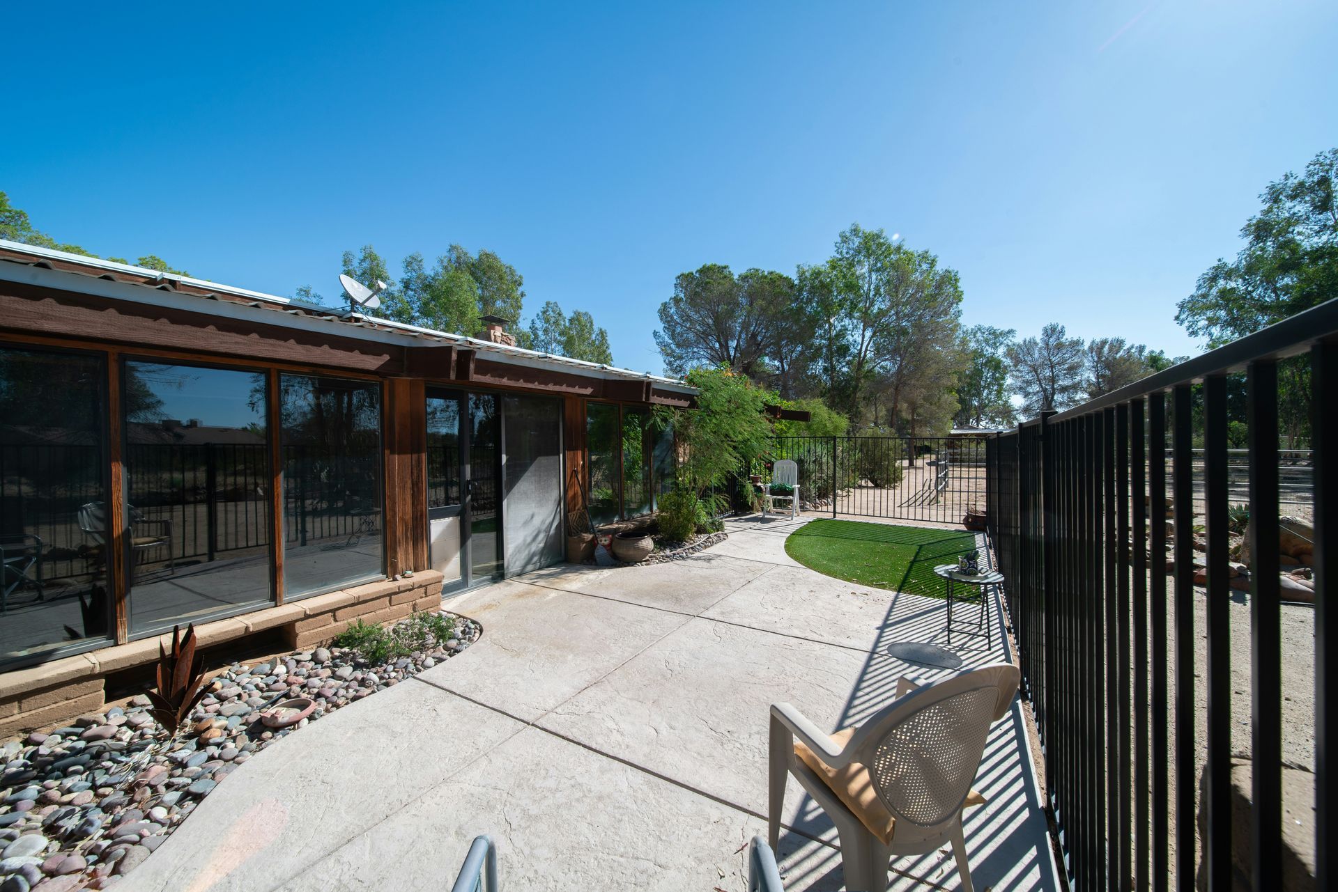 Courtyard with concrete path, chairs, black fence, and modern building under clear blue sky