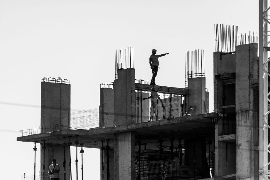Construction worker standing on a high-rise building under construction, silhouetted against the sky