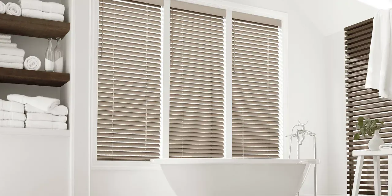 There is a bathtub in the bathroom with blinds on the windows.