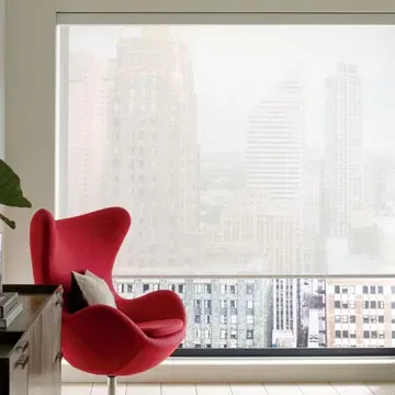 A red chair is sitting in front of a window with a view of a city.
